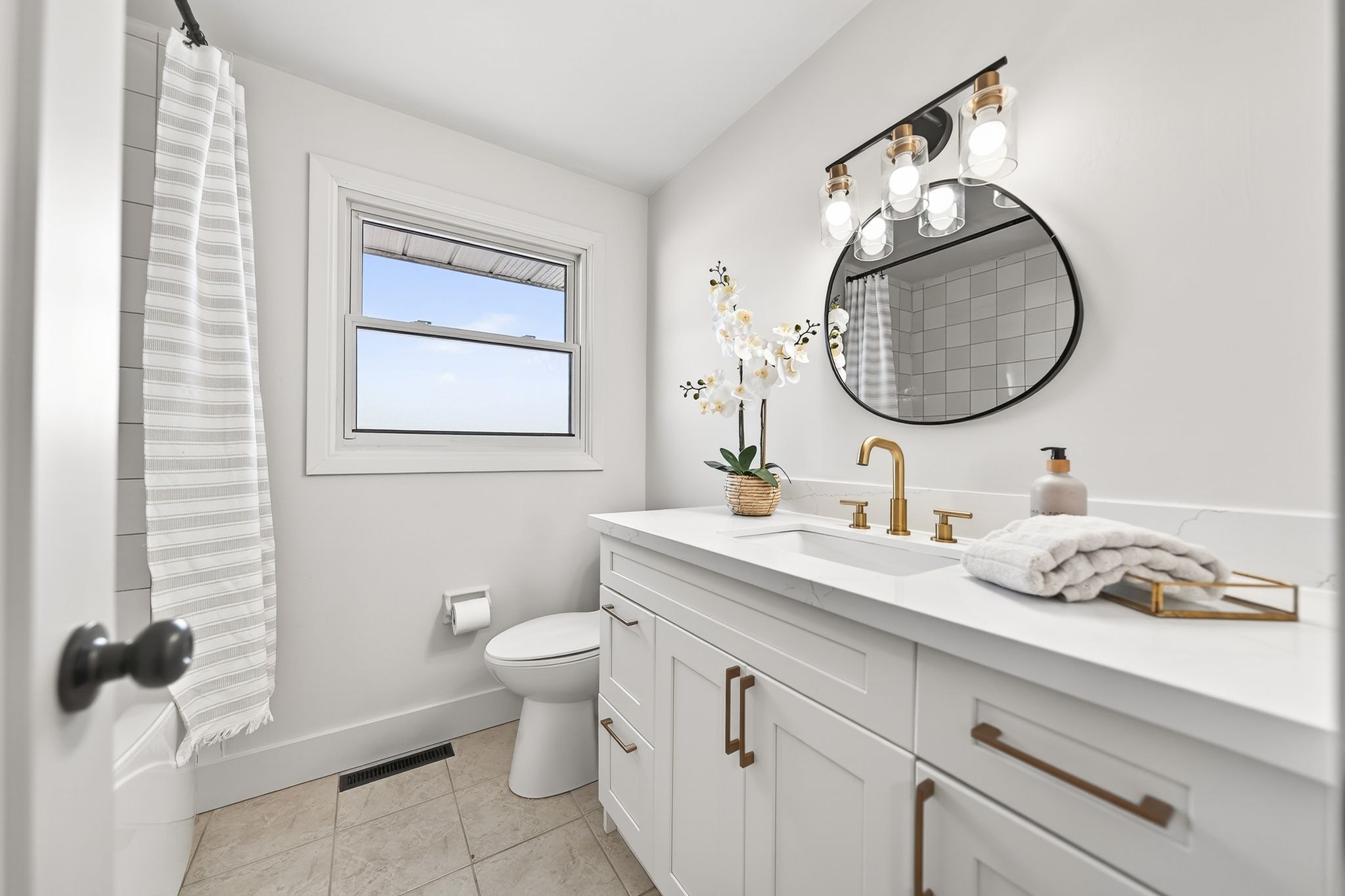 Cambridge house refresh — updated bathroom with new shaker vanity, quartz countertop, gold fixtures, black round mirror and updated light bar